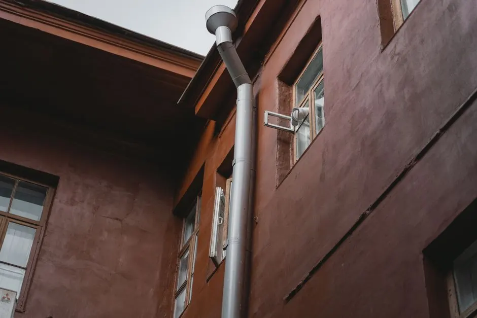 A brown building exterior with pipes and windows, photographed from a low angle.