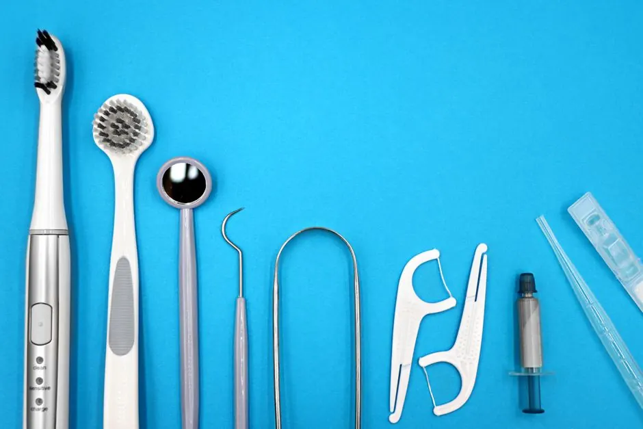 Flat lay of dental care tools including toothbrushes, dental mirror, and floss sticks on blue background.