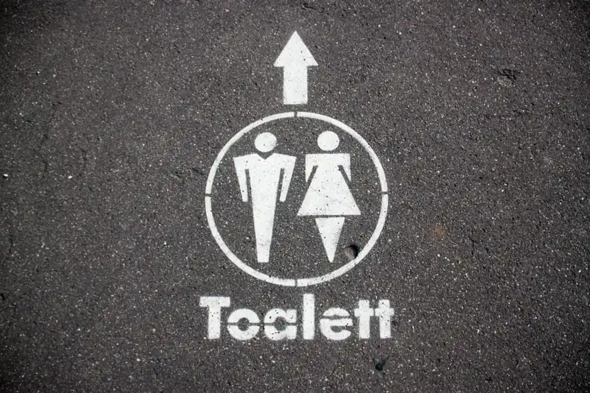 Road marking indicating direction to public toilets on asphalt pavement.